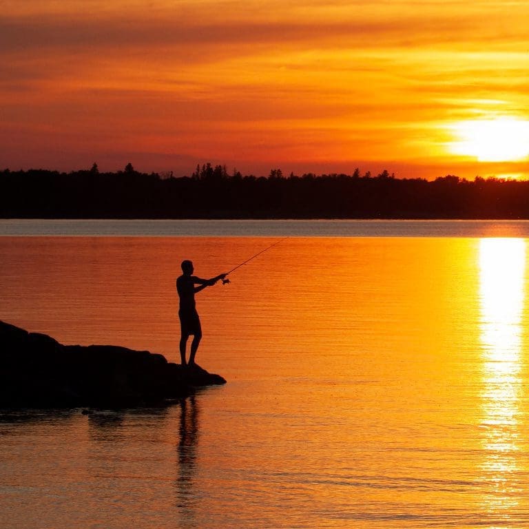 Man fishing off a dock at sunset