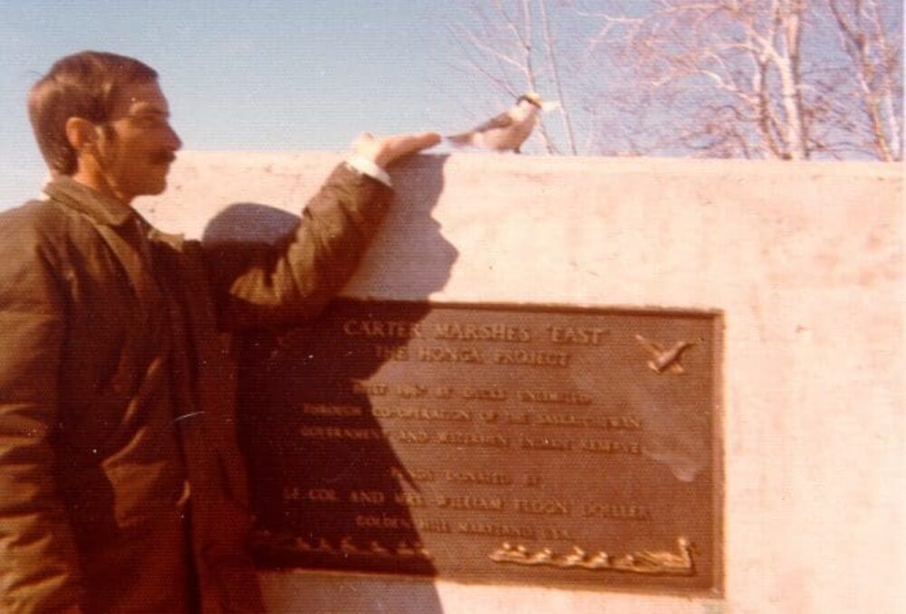 Dale Brydges poses with a feathered friend at a cairn and plaque at the Carter Marshes in Saskatchewan, 1976. 
