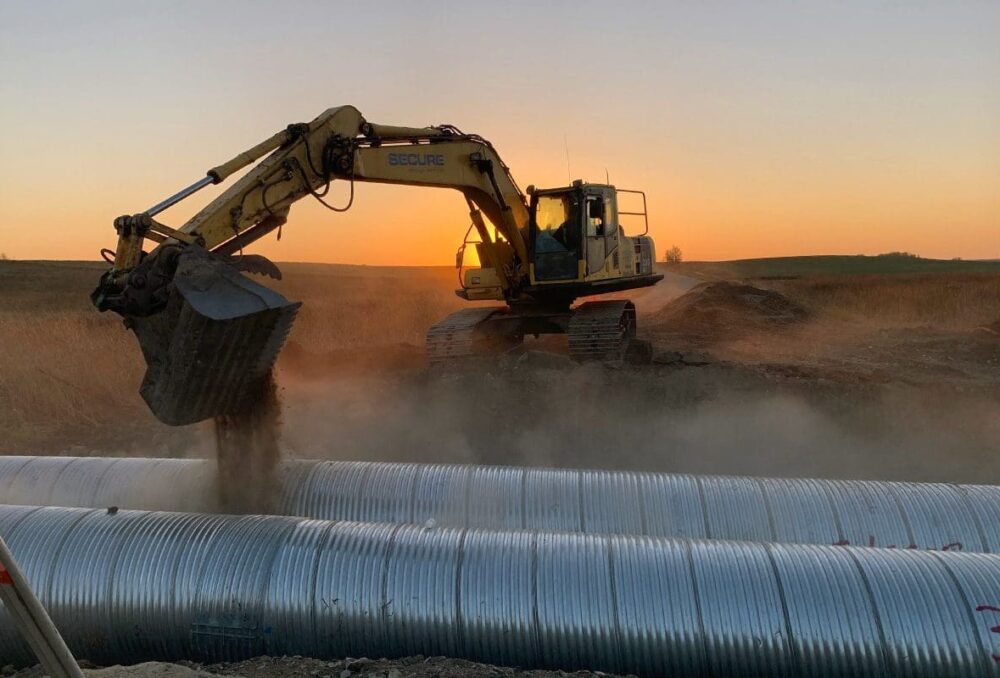 A backhoe buries pipes at the DUC project at Bars Lake near Kenton, Man.