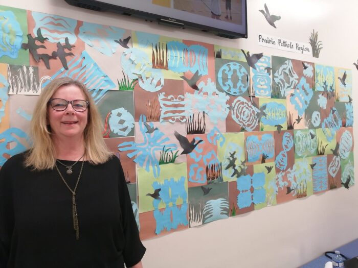 Artist-in-residence Diana Roelens stands next to student art installation, A Bird's Eye View of the Prairie Pothole Region