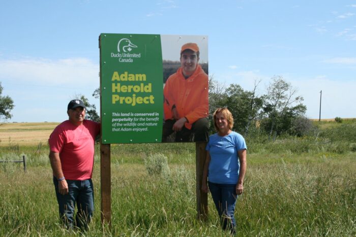 Russell and Raelene Herold stand by the sign at the entrance to habitat lands conserved in memory of Adam.