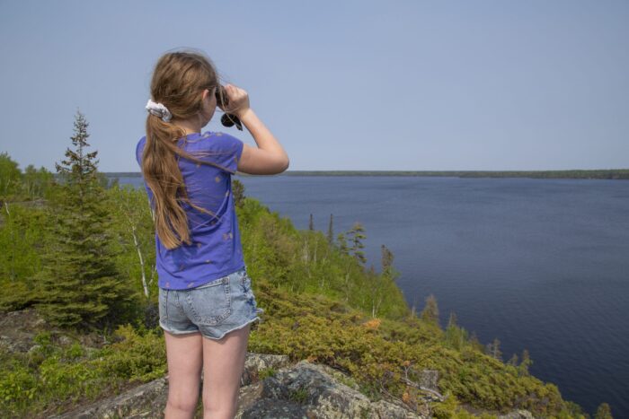 Young girl with binoculars near a boreal lake. 